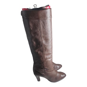 May include: A pair of brown leather knee-high boots with a pointed toe and a low heel.