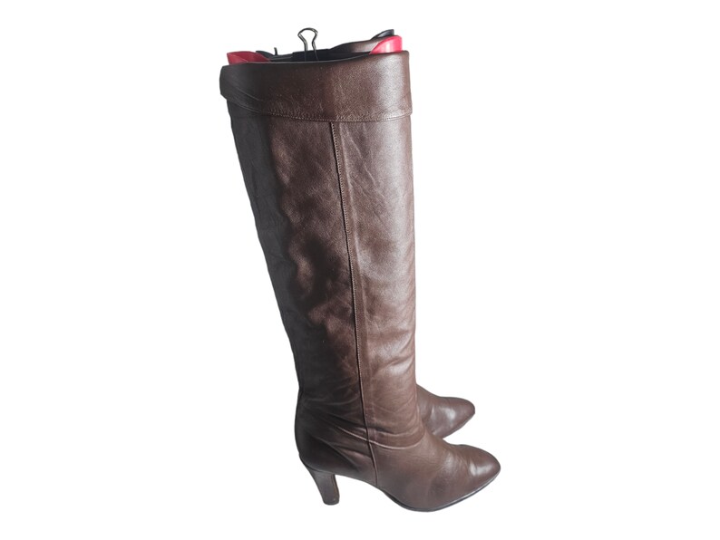 May include: A pair of brown leather knee-high boots with a pointed toe and a low heel.