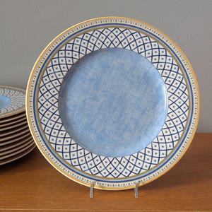 May include: A blue and white ceramic dinner plate with a gold rim and a geometric pattern. The plate has a light blue center with a subtle textured finish.