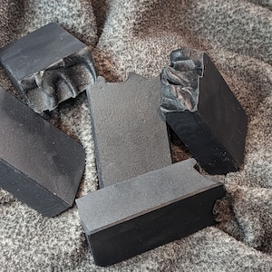 May include: Five black bars of soap, some with chipped edges, are arranged on a gray, textured surface.
