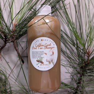 Può includere: Una bottiglia marrone di "Golden Goat Pink Tar Shampoo" con tappo bianco ed etichetta con illustrazione di capra. La bottiglia è da 591 ml ed è circondata da aghi di pino verdi.