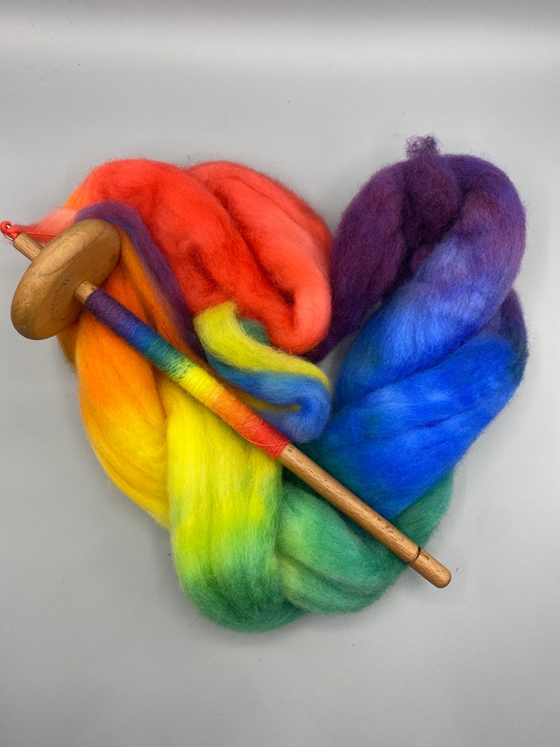 May include: Rainbow colored wool roving arranged in a heart shape with a wooden spinning wheel spindle.