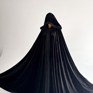 Dramatic black velvet witch cloak with oversized hood inspired by gothic Halloween fashion and fantasy cosplay aesthetics. Handmade hooded cape with elegant flowing shape and premium velvet texture designed for vampire costumes, dark feminine styling, renaissance fairs and cinematic photoshoots. Floor length silhouette creates powerful luxury gothic appearance.