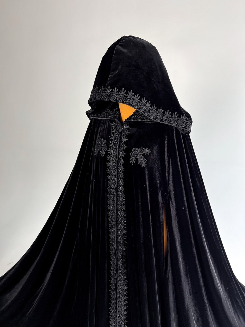Handmade black velvet cloak with hood and hidden arm openings designed for comfortable movement during Halloween parties, gothic events and fantasy cosplay. Medium weight velvet fabric creates rich folds and luxurious texture while remaining comfortable to wear. Elegant hooded witch cape inspired by vampire aesthetics, medieval fantasy and gothic fashion trends.