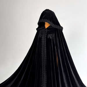 Black velvet Halloween cloak with oversized hood and luxurious flowing silhouette inspired by fantasy fashion and gothic aesthetics. Handmade floor length cape for witch costume, vampire outfit and dark fantasy cosplay. Medium density velvet fabric creates rich elegant folds and premium texture while maintaining comfort during events and photoshoots.