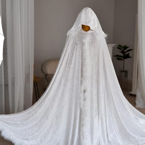 Elegant white velvet fantasy cape with oversized hood and decorative feather trim inspired by medieval and fantasy aesthetics. Handmade full length cloak with luxurious soft velvet texture and dramatic flowing silhouette perfect for cosplay, artistic photoshoots, fantasy styling and renaissance inspired fashion looks.