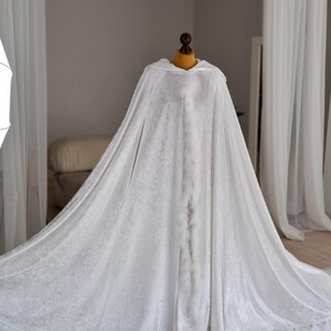 Soft white velvet fantasy cloak with oversized hood and decorative feather trim inspired by elegant medieval and fantasy fashion. Handmade flowing cape with dramatic full length silhouette and luxurious velvet texture created for artistic photography, cosplay styling, fantasy aesthetics and renaissance inspired looks.