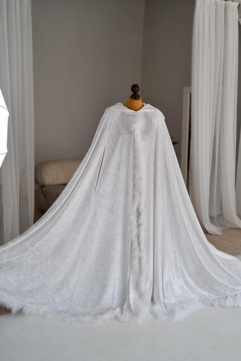 Soft white velvet fantasy cloak with oversized hood and decorative feather trim inspired by elegant medieval and fantasy fashion. Handmade flowing cape with dramatic full length silhouette and luxurious velvet texture created for artistic photography, cosplay styling, fantasy aesthetics and renaissance inspired looks.