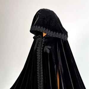 Premium black velvet hooded cape with gothic fantasy inspired silhouette and luxurious flowing movement. Handmade Halloween cloak designed individually for each customer according to height and preferred length. Elegant witch cloak with hidden arm slits and soft medium weight velvet fabric perfect for cosplay, vampire outfits and gothic themed events.