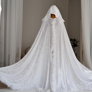 White velvet hooded cape with decorative feather trim and elegant flowing silhouette designed for fantasy aesthetics and artistic styling. Handmade unisex fantasy cloak with oversized hood and luxurious velvet texture perfect for cosplay, renaissance fairs, medieval inspired outfits and themed photoshoots.