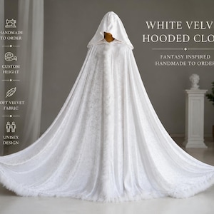 White velvet hooded cloak with decorative feather trim and elegant flowing silhouette inspired by fantasy aesthetics and medieval fashion. Handmade unisex fantasy cape with oversized hood, soft velvet texture and dramatic full length design created for cosplay, artistic photoshoots, renaissance fairs, fantasy styling and cinematic looks.