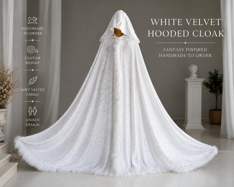 White velvet hooded cloak with decorative feather trim and elegant flowing silhouette inspired by fantasy aesthetics and medieval fashion. Handmade unisex fantasy cape with oversized hood, soft velvet texture and dramatic full length design created for cosplay, artistic photoshoots, renaissance fairs, fantasy styling and cinematic looks.