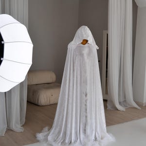 Handmade white velvet fantasy cape with dramatic oversized hood and decorative feather trim. This elegant unisex cloak features luxurious flowing silhouette, soft velvet texture and fantasy inspired aesthetic ideal for artistic photography, cosplay styling, renaissance fairs and medieval inspired fashion looks.