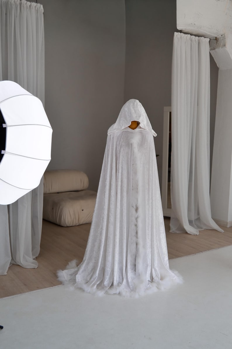 Handmade white velvet fantasy cape with dramatic oversized hood and decorative feather trim. This elegant unisex cloak features luxurious flowing silhouette, soft velvet texture and fantasy inspired aesthetic ideal for artistic photography, cosplay styling, renaissance fairs and medieval inspired fashion looks.