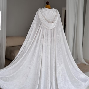 Handmade white velvet hooded cloak inspired by fantasy fashion and elegant medieval silhouettes. This unisex full length fantasy cape features decorative feather trim, dramatic oversized hood and soft flowing velvet fabric that reflects light beautifully and creates a luxurious cinematic appearance for cosplay and photoshoots.