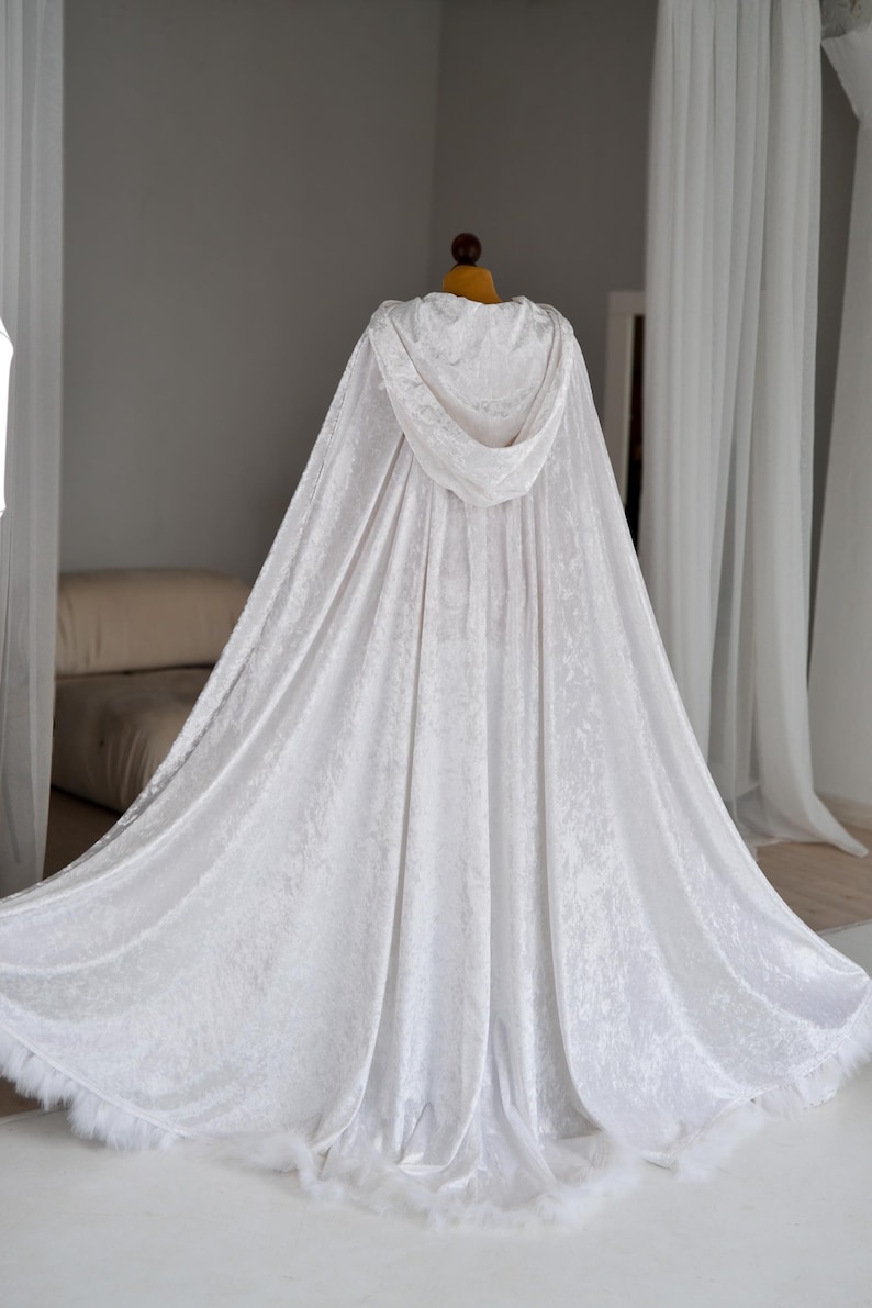 Handmade white velvet hooded cloak inspired by fantasy fashion and elegant medieval silhouettes. This unisex full length fantasy cape features decorative feather trim, dramatic oversized hood and soft flowing velvet fabric that reflects light beautifully and creates a luxurious cinematic appearance for cosplay and photoshoots.