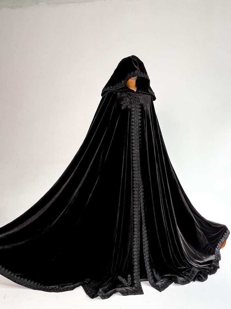 Black velvet hooded cloak for women and men inspired by gothic fashion, Halloween aesthetics and dark fantasy style. Floor length handmade velvet cape with oversized hood, hidden arm slits and elegant flowing silhouette. Premium medium weight velvet cloak designed for witch costume, vampire outfit, gothic cosplay, renaissance fair clothing and dramatic fantasy photoshoots.