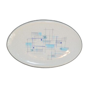 May include: An oval-shaped white serving platter featuring a speckled finish and a central graphic pattern of intersecting thin blue lines, light blue rectangular blocks, and small starburst shapes arranged in a scattered, geometric composition.
