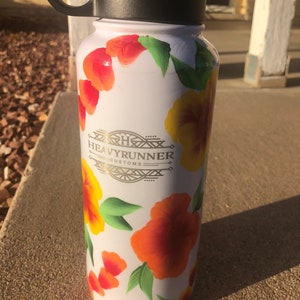 May include: White water bottle with a black lid and handle. The bottle is decorated with hand-painted orange, yellow, and red flowers. The text "Heavyrunner Customs" is printed in gold on the bottle.