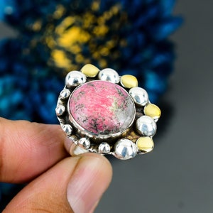 Peut inclure: Une bague en argent avec une pierre précieuse rose et grise sertie dans une bélière en argent et or. La bague est entourée d'un cercle de perles en argent et or.