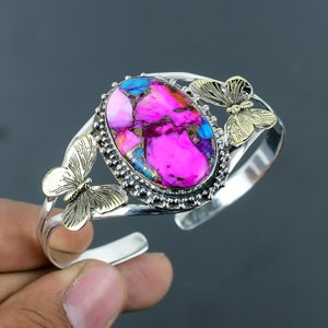 Pode incluir: Um bracelete de prata com um design de borboleta rosa, azul e dourado. O bracelete apresenta uma pedra grande de forma oval com um padrão marmorizado rosa, azul e dourado.