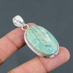 Op de afbeelding: Een zilveren hanger met een ovale, groen-witte edelsteen. De hanger is gezet in een zilveren bezel en heeft een lus om een ketting aan te bevestigen.