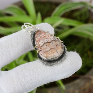 May include: A silver pendant with a teardrop-shaped, multi-colored agate stone set in a silver bezel. The stone has brown, pink, and white stripes. The pendant is accented with gold wire wrapping around the stone.