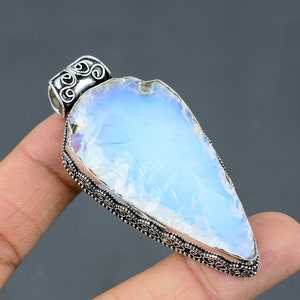 May include: A silver pendant with a white opal gemstone in a teardrop shape. The pendant has an intricate silver design around the edge.