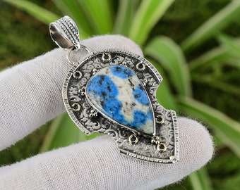 Könnte beinhalten: Ein silberner Anhänger mit einem komplizierten Design, das einen blauen und weißen Edelstein zeigt. Der Anhänger hat eine Tropfenform und ist in einen silbernen Rahmen mit goldenen Akzenten gefasst.