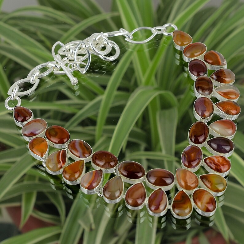 May include: A silver necklace with a brown agate stone pendant. The necklace is made of silver chain and has a clasp closure. The agate stone is a natural stone with a unique pattern.