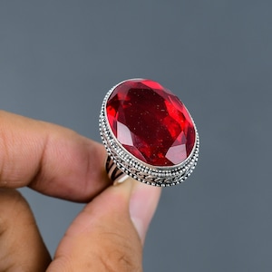 May include: A silver ring with a large, oval-shaped, red gemstone. The ring has a detailed, ornate design around the gemstone.