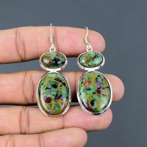 May include: A pair of silver earrings with green and gold oval-shaped gemstones. The gemstones have a mosaic-like pattern with red, green, and gold flecks.