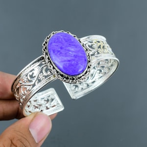 Pode incluir: Um bracelete de prata com um design ornamentado e uma grande pedra oval de cor púrpura.