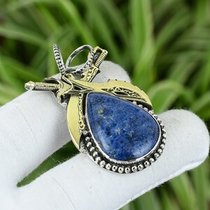 Puede incluir: Un colgante de plata y oro con una piedra de lapislázuli azul engastada en un diseño detallado de espadas cruzadas.