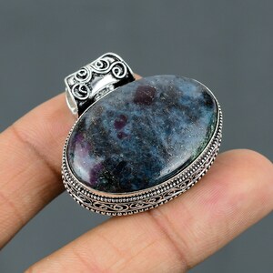 May include: A silver pendant featuring an oval blue and green gemstone with red flecks. The pendant has an ornate silver border and a bail with a swirl design.