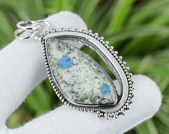 Puede incluir: Un colgante de plata con una piedra de cianita azul y blanca engastada en un marco ovalado de plata. El colgante tiene un borde de cuentas y un bucle para sujetar una cadena.