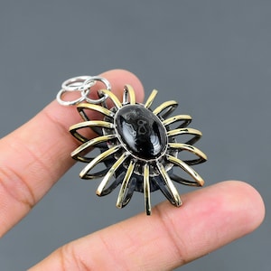 May include: A silver and gold pendant featuring a black oval gemstone surrounded by a sunburst design.