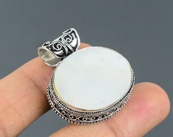 May include: A white mother of pearl pendant with an ornate silver frame. The pendant is oval shaped and has a silver bail.