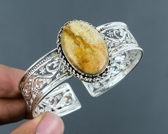 May include: A silver cuff bracelet with an oval-shaped brown and white gemstone set in a silver bezel. The bracelet has a delicate floral design.