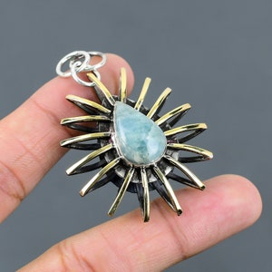 May include: A silver and gold pendant with a teardrop-shaped aquamarine gemstone set in a sunburst design.