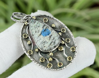 Puede incluir: Un colgante de plata con una piedra moteada azul y blanca engastada en un diseño de filigrana de plata y oro.