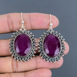 Peut inclure: Une paire de boucles d'oreilles en argent avec des pierres précieuses ovales, violet foncé. Les pierres précieuses sont entourées d'un travail de métal décoratif argenté et doré. Les boucles d'oreilles ont une fermeture à crochet.