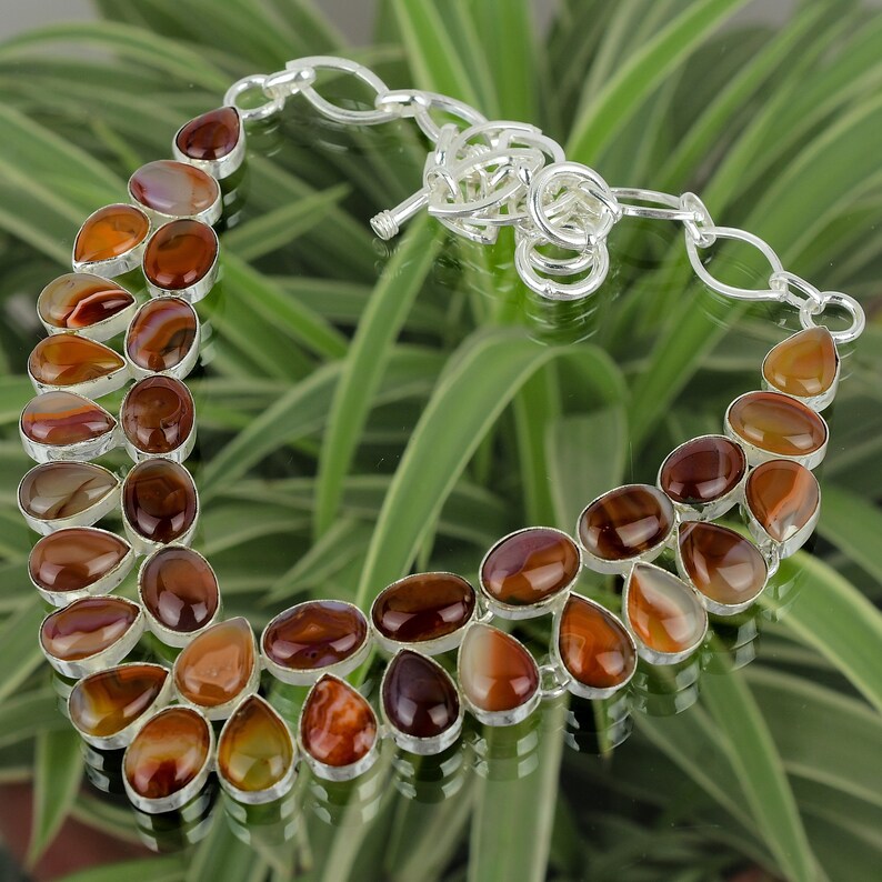 May include: A silver necklace with a teardrop-shaped agate stone design. The stones are a mix of brown, orange, and white.