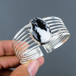 May include: A silver cuff bracelet with a black and white oval gemstone. The bracelet has a multi-strand design with five bands.