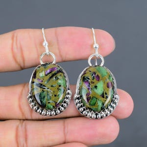 May include: A pair of silver earrings with oval-shaped green and purple gemstone stones. The stones are set in a silver bezel and surrounded by a row of silver beads.