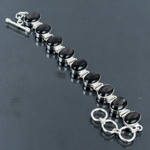 May include: A silver bracelet featuring black oval-shaped stones. The bracelet has a clasp and is made of a chain link design.