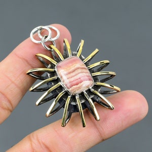 May include: A silver and gold pendant featuring a pink and white striped gemstone set in a sunburst design.