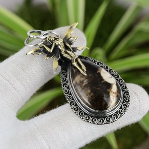 May include: A silver pendant with a brown and white agate stone and a gold-toned fairy figure.