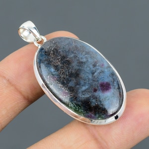 May include: A silver pendant with a blue, green, and black oval gemstone. The gemstone has a speckled pattern and is set in a silver bezel.
