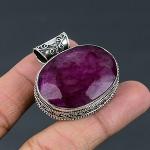 May include: A silver pendant featuring an oval-shaped, deep purple gemstone set within a silver filigree frame.